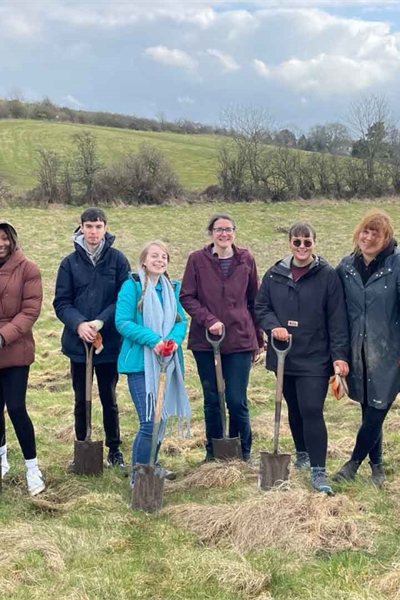 Strathclyde students and staff in the countryside, holding tree planting equipment and smiling at the camera.