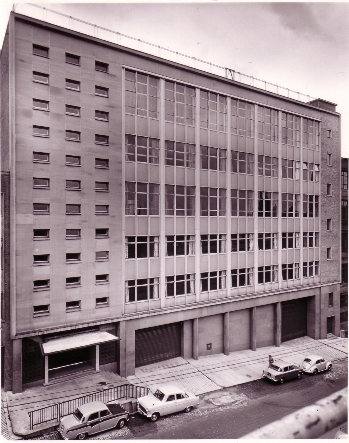 An old photograph in aged purple tone greyscale, showing the John Street building with vintage cars parked outside
