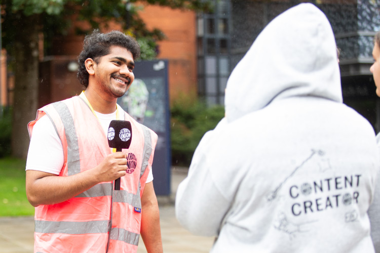 Student holding a Strath Union microphone, smiling at person wearing a Strath Content Creator hoody.