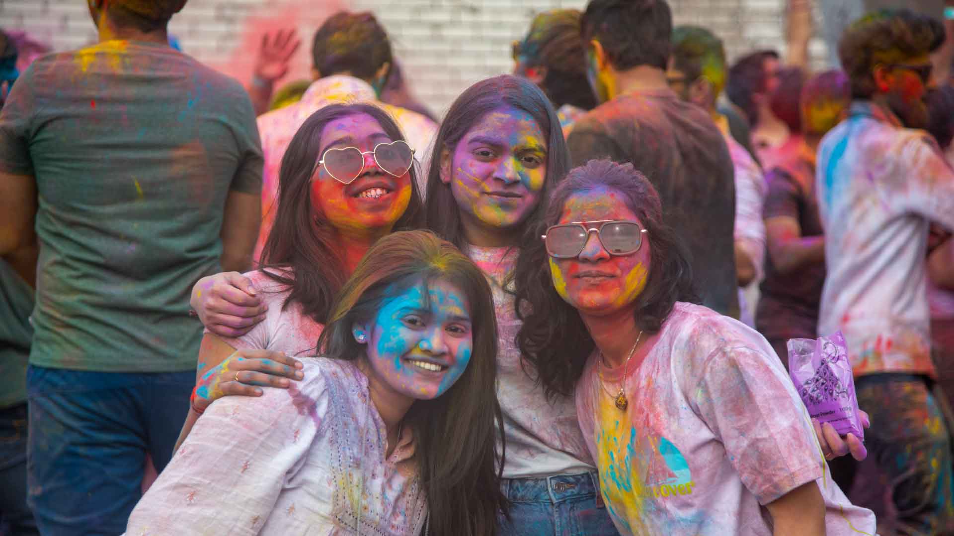 Students with colourful powder on their faces, smiling and embracing, posing for the camera