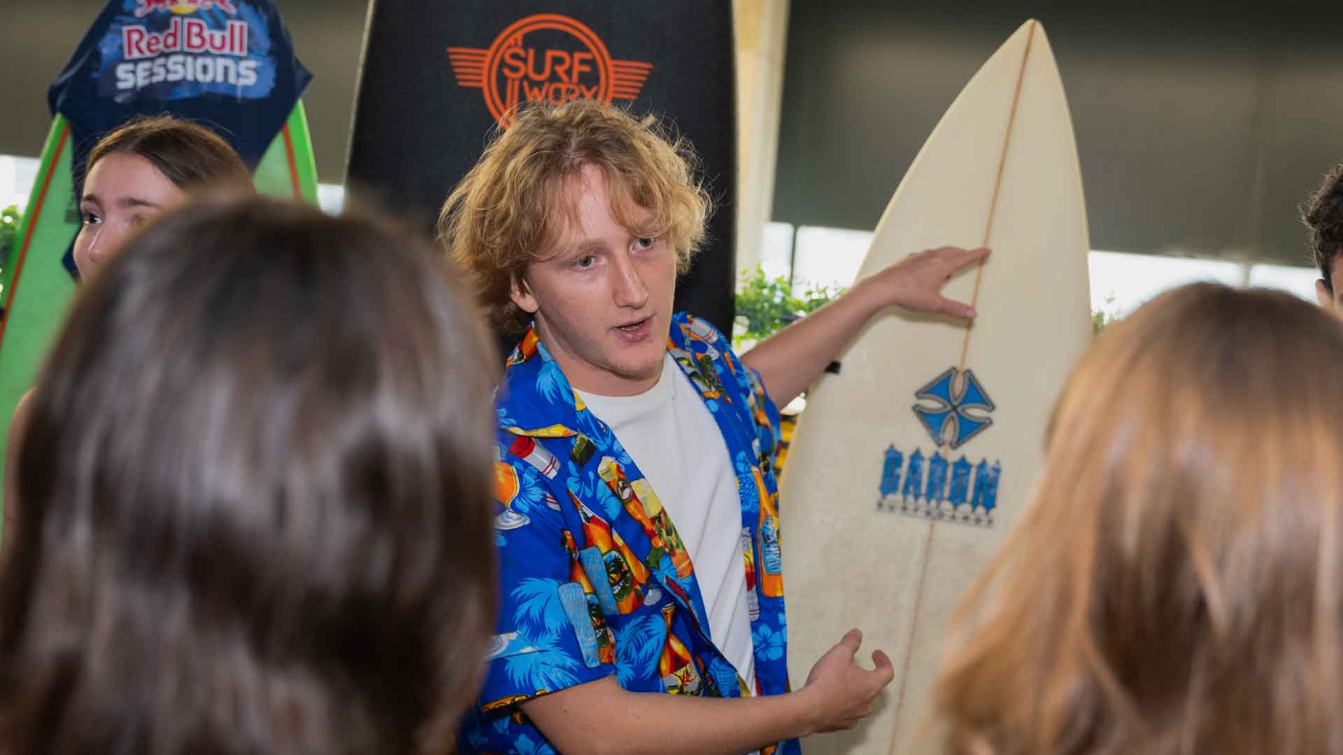 Student talking to other students while pointing to a surfboard.