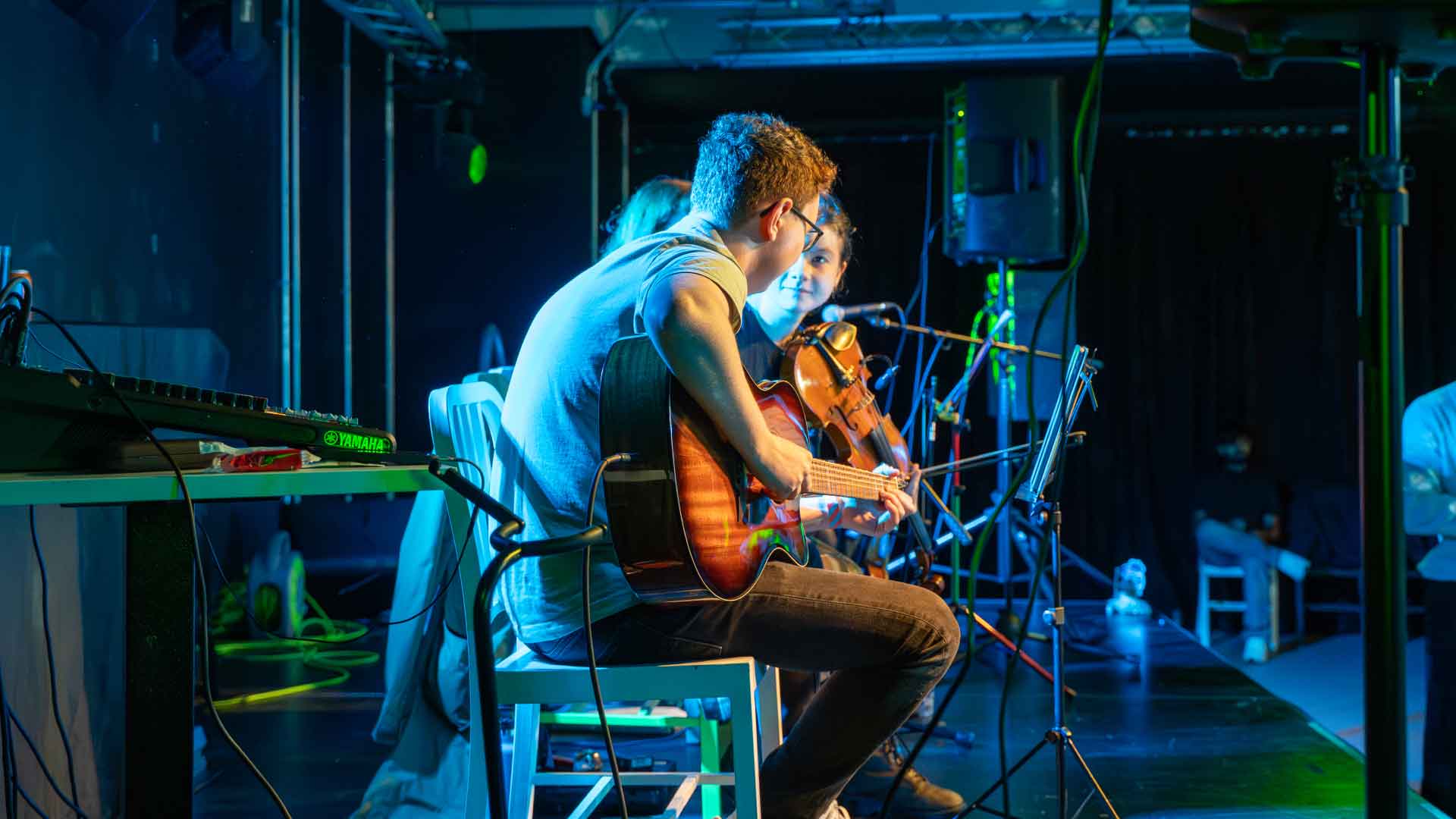 Students on stage, playing the guitar and the violin.