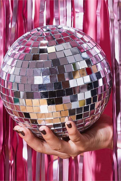A person holding a disco ball against pink glittery curtains