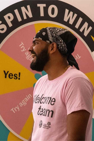 Person wearing a pink Welcome Team t-shirt, standing in front of a "Spin to Win" wheel.