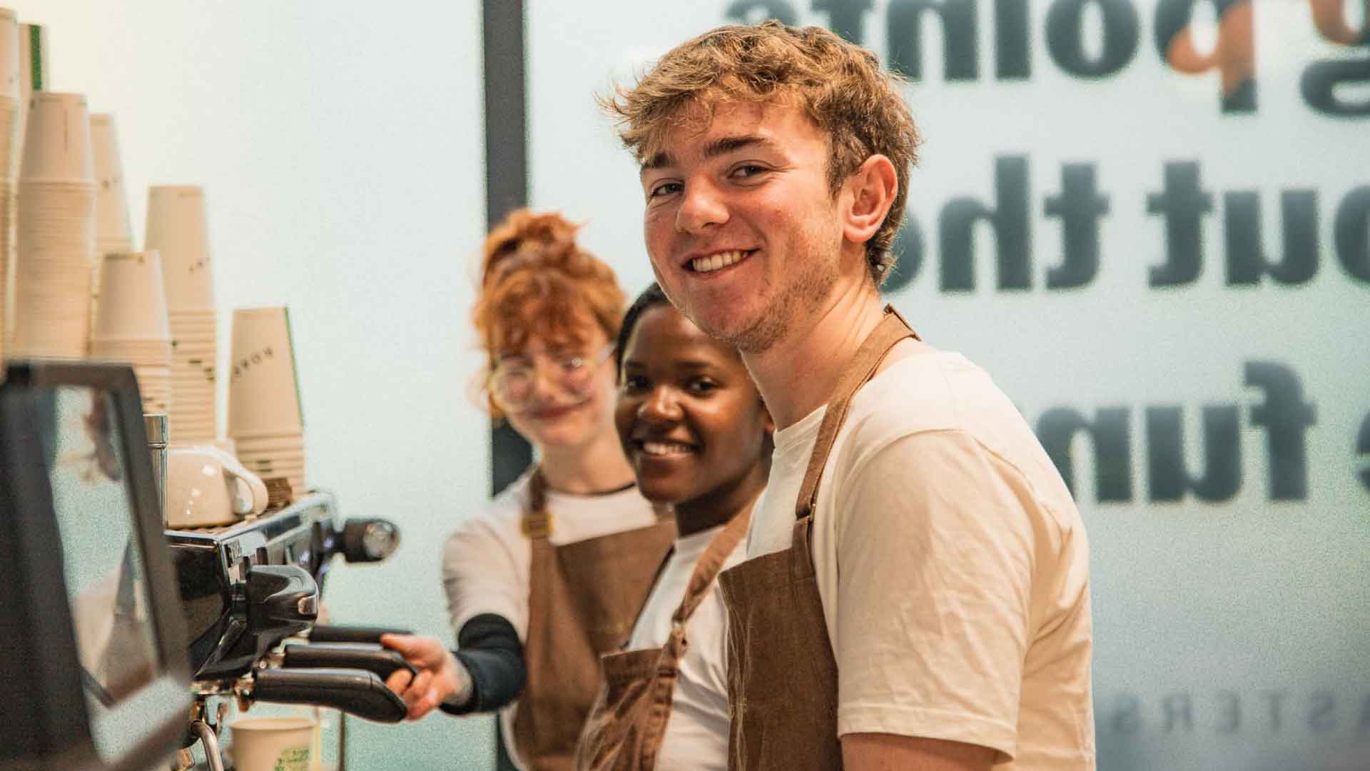 Student staff at Roasters cafe, smiling at the camera.