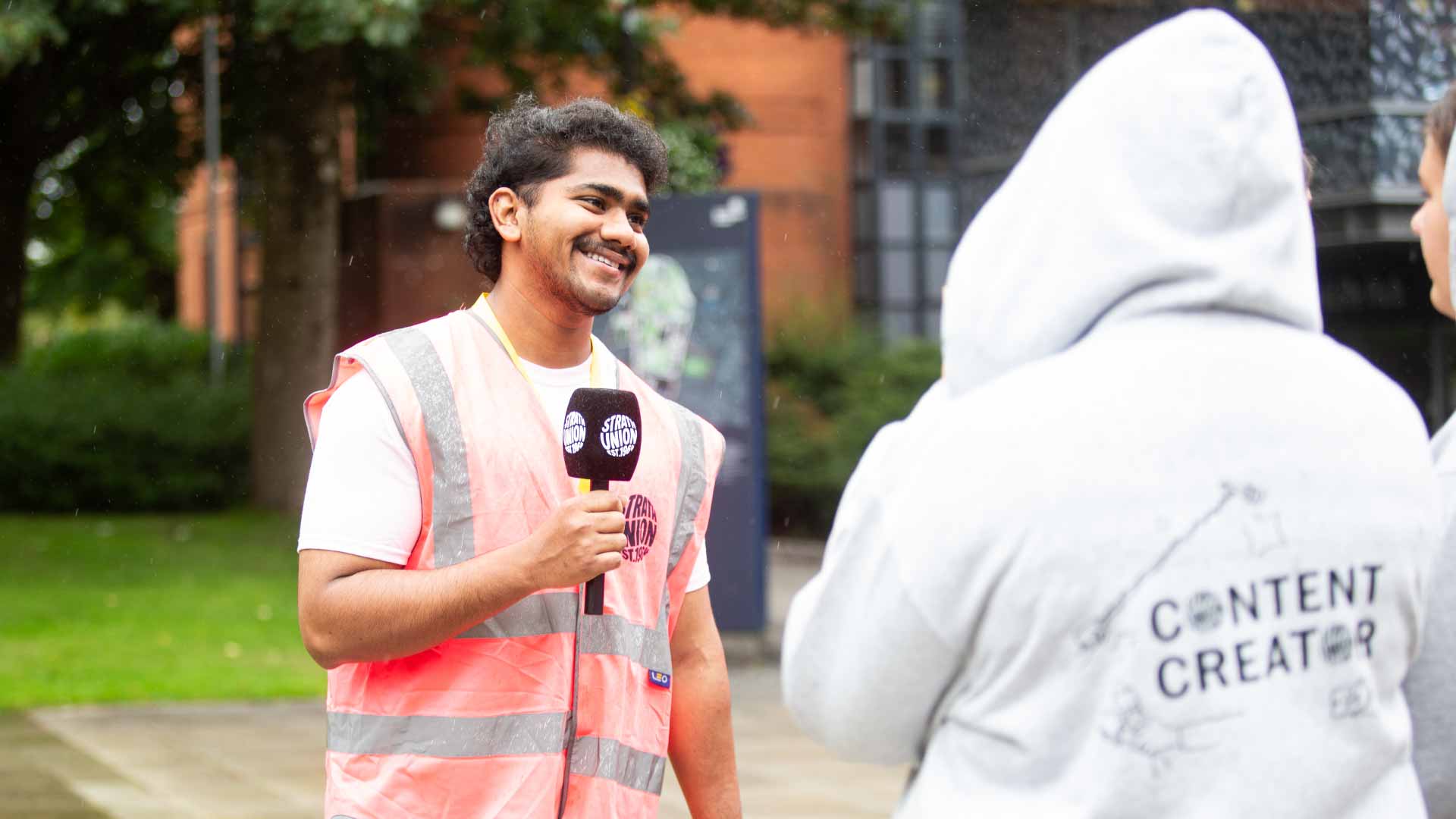 Person holding Strath Union microphone and smiling to person wearing "content creator" hoody.