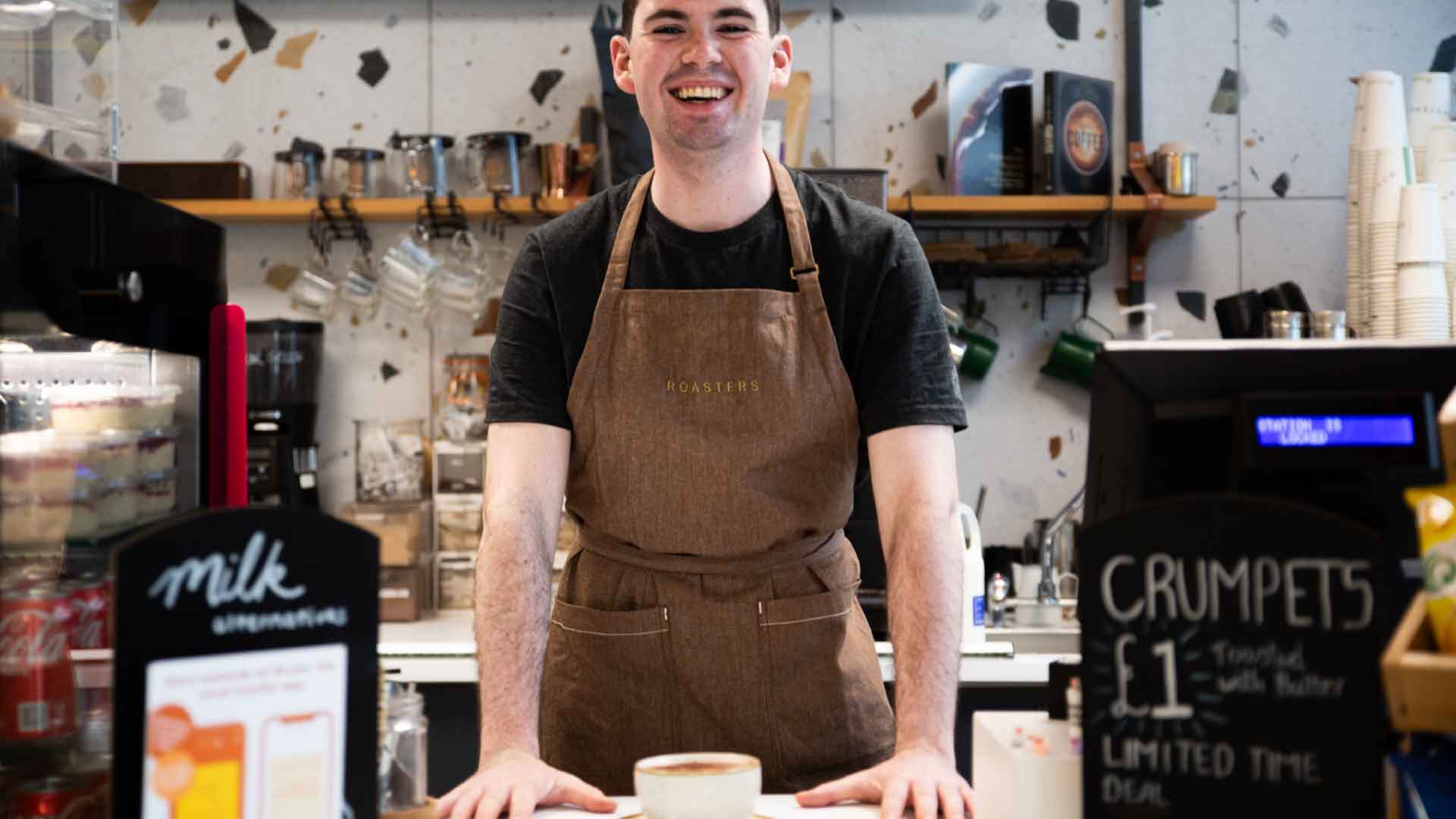 Student staff at Roasters cafe, smiling at the camera from behind the counter.