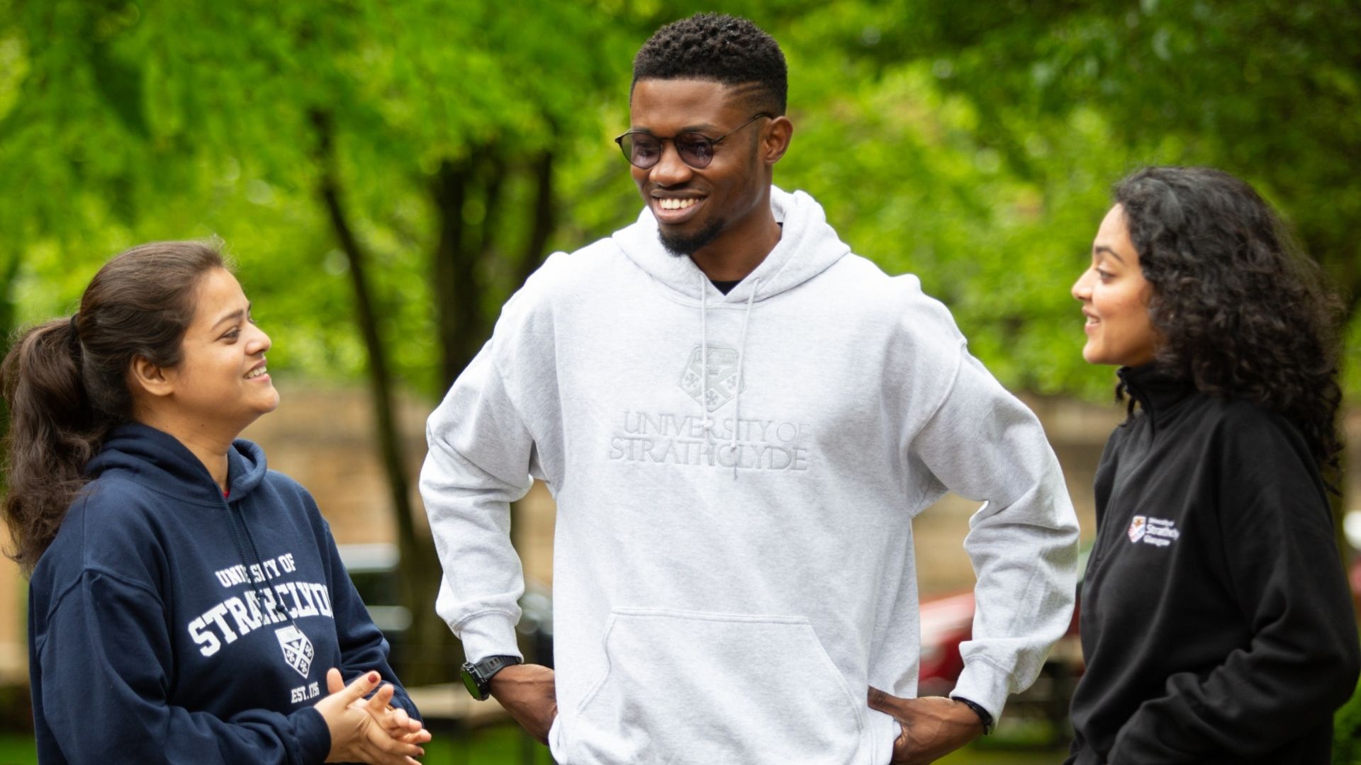 Three students smiling and chatting, wearing University of Strathclyde hoodies in various colours