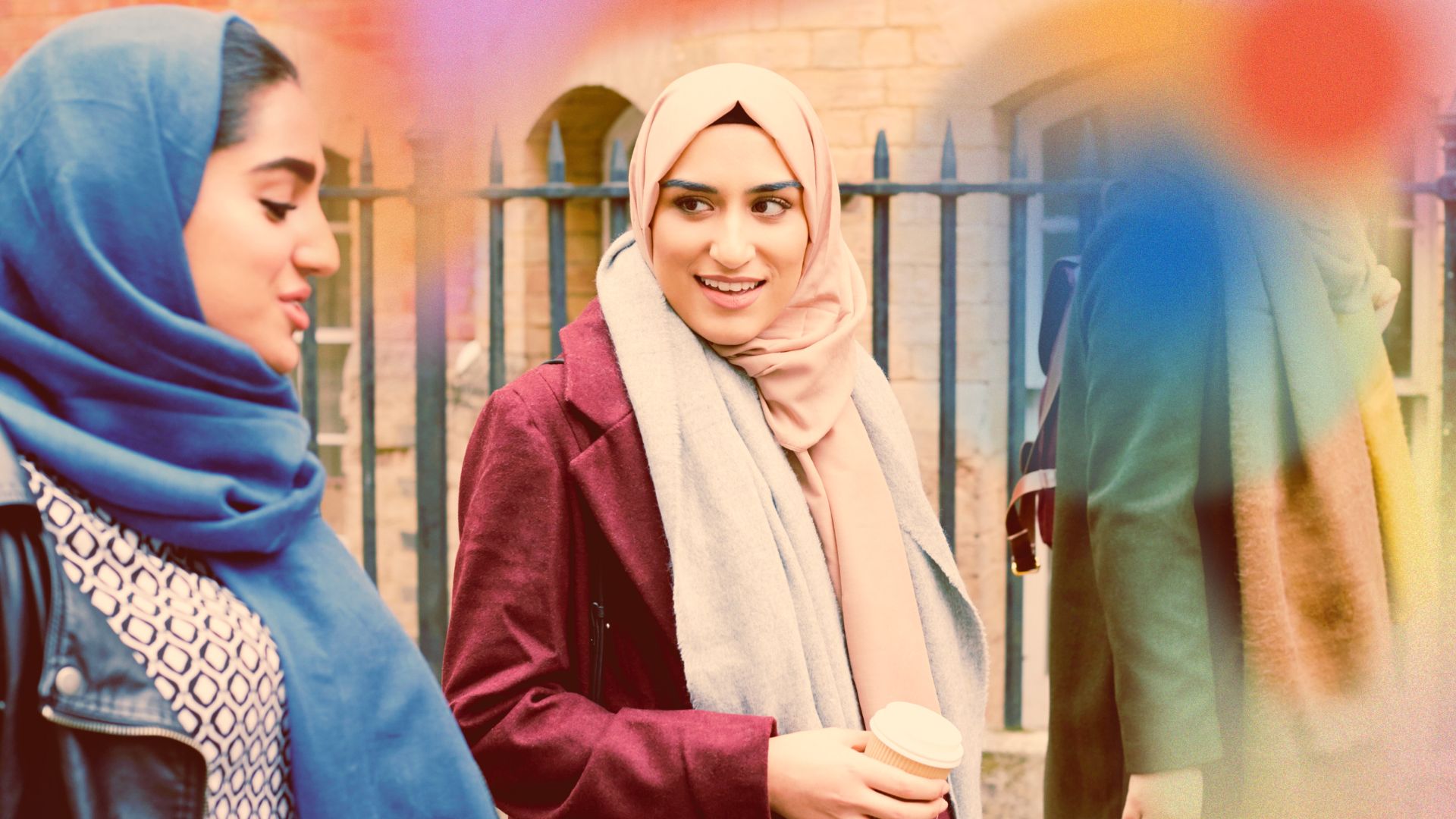 Two people walking while chatting in an urban setting. One of them is holding a coffee.