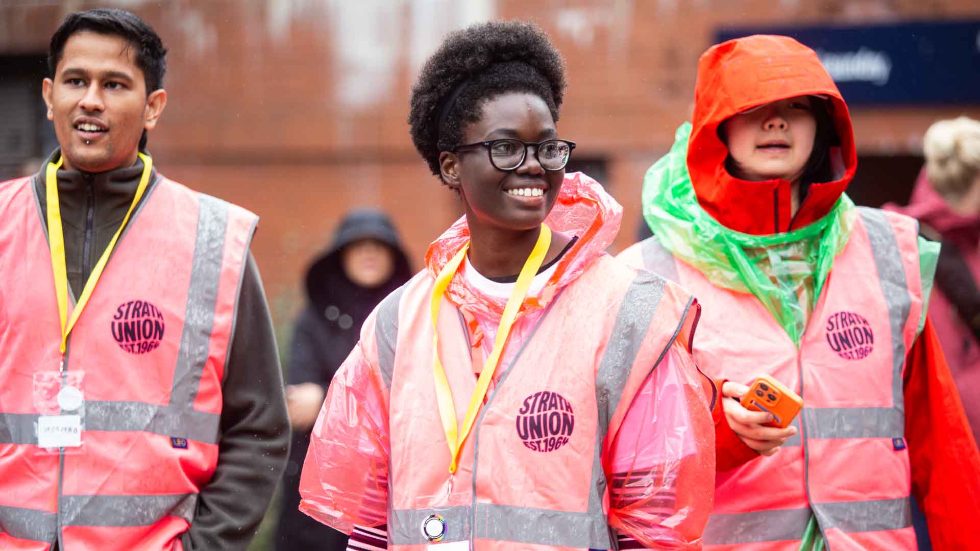 Members of the Strath Union Welcome Team, wearing high vis jackets and smiling, a crowd of people in the background.