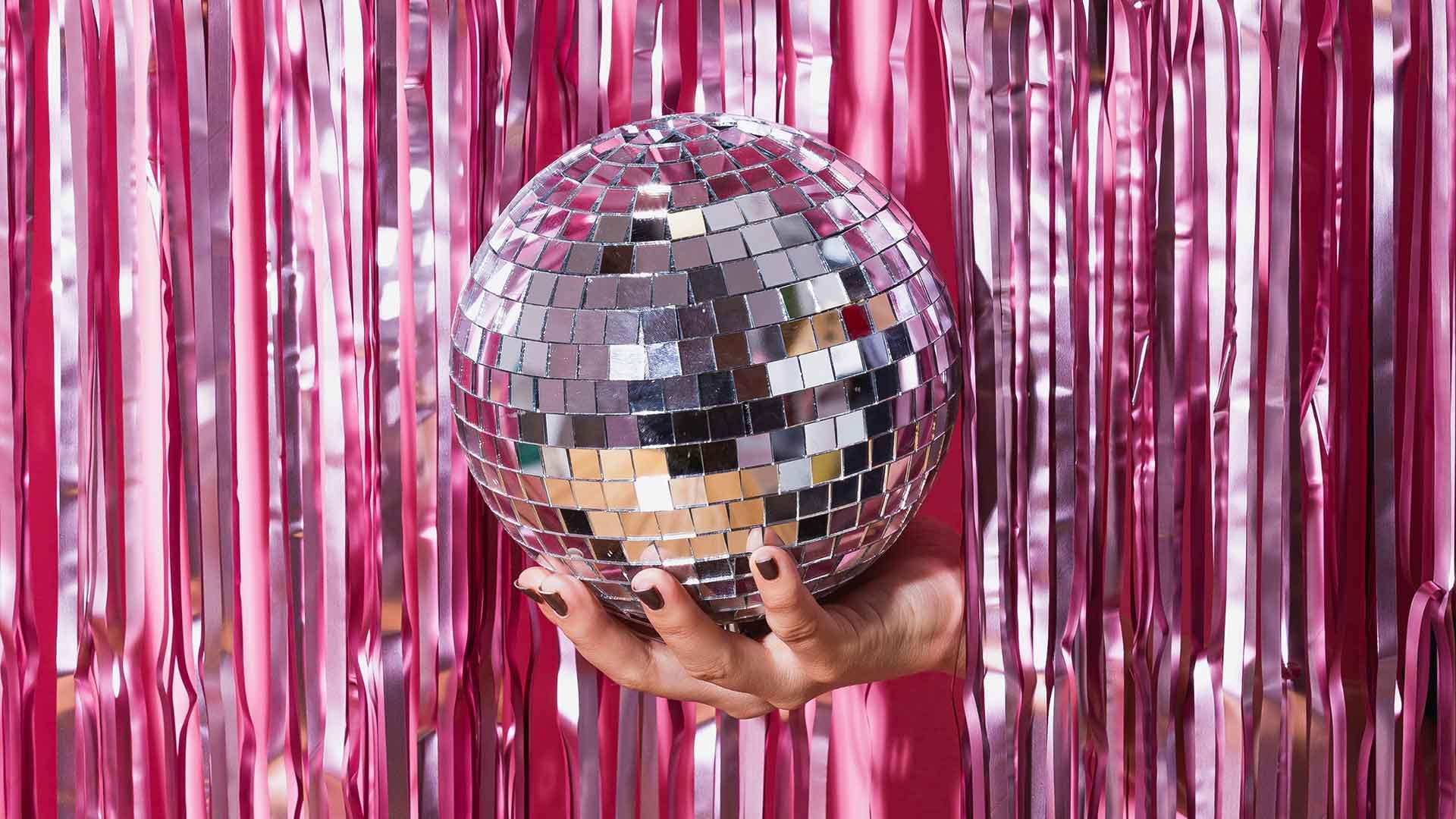 Disco ball held by hand coming out of pink curtain