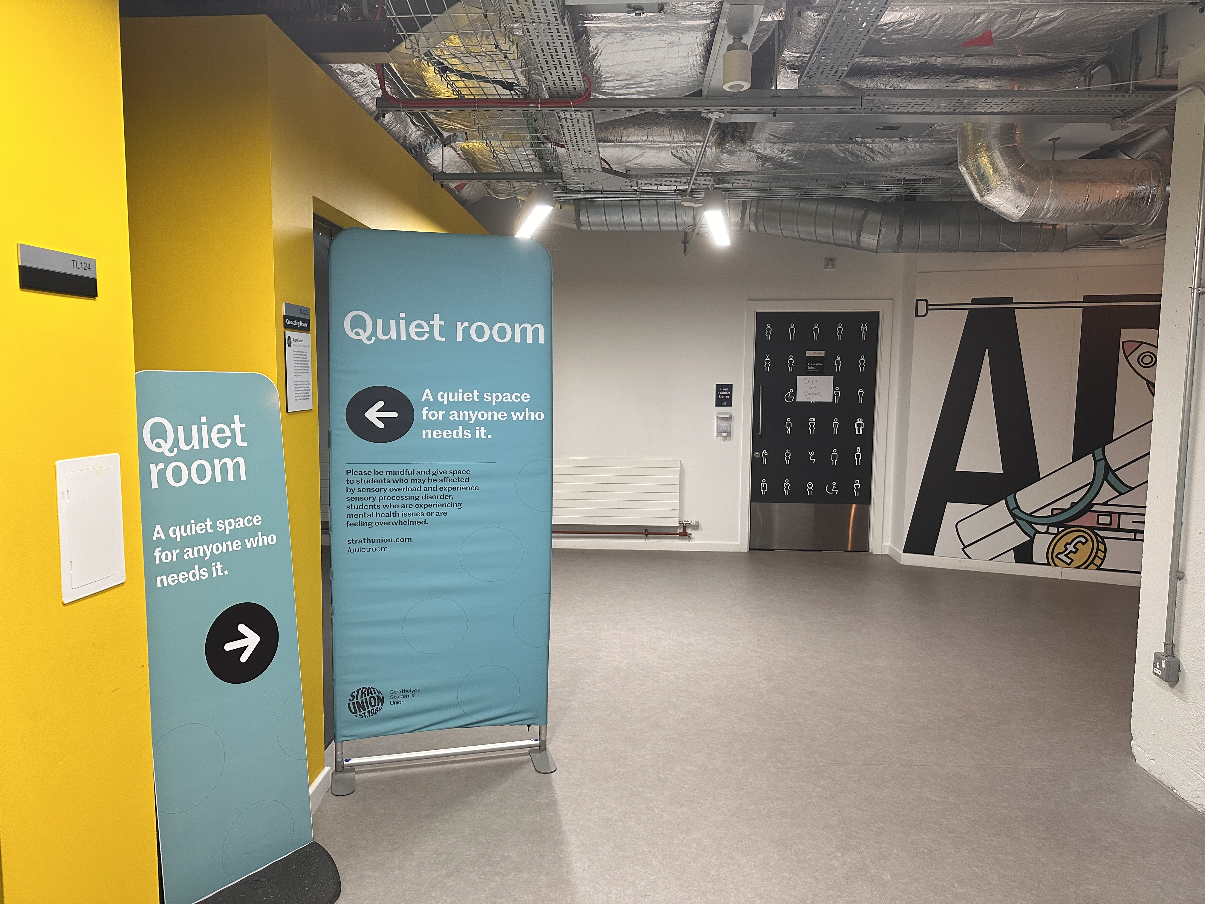 Back corner of level 1 concourse with turquoise signage for the quiet room.