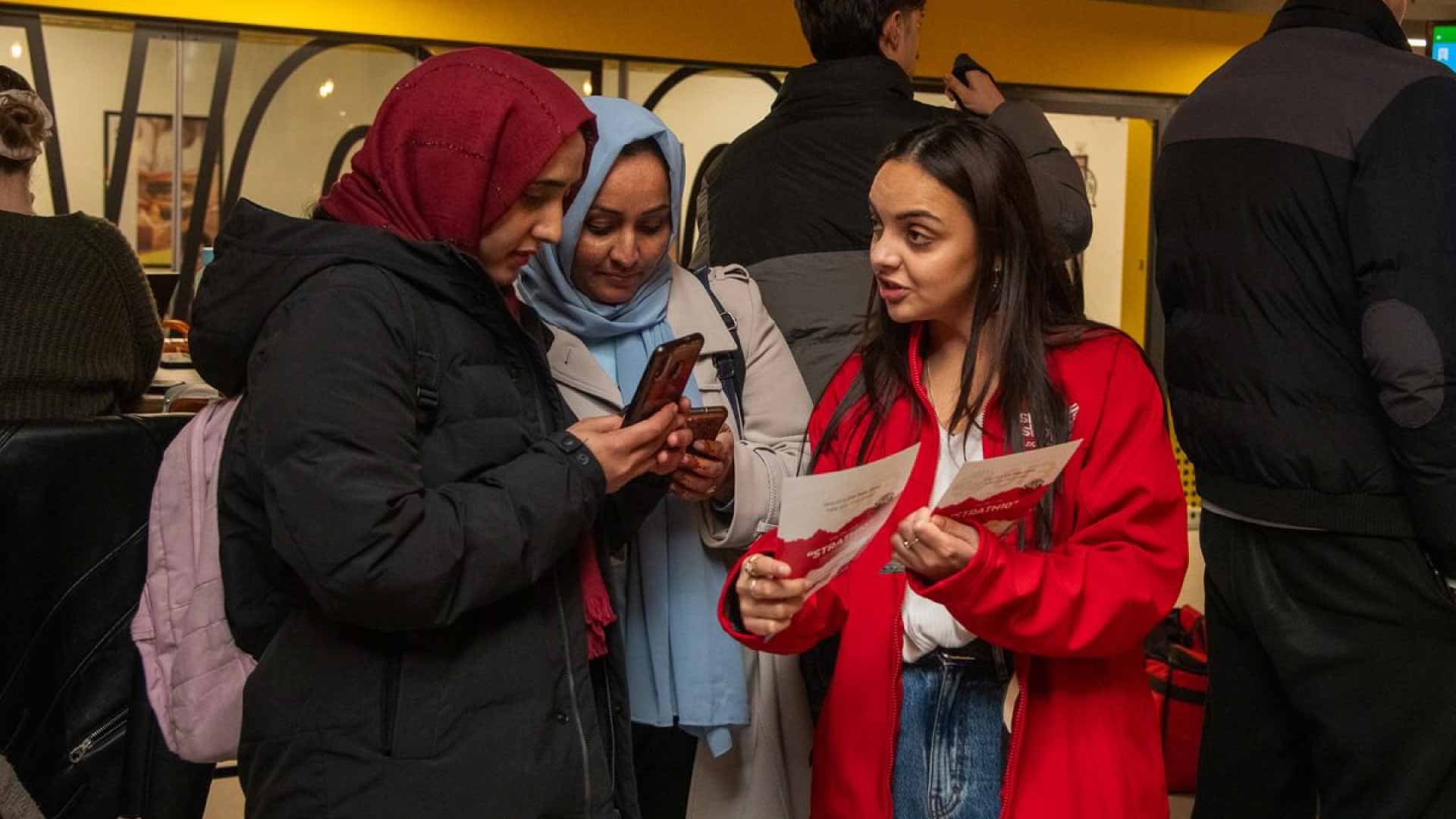 Advertiser holding promotional flyers and talking to two students.