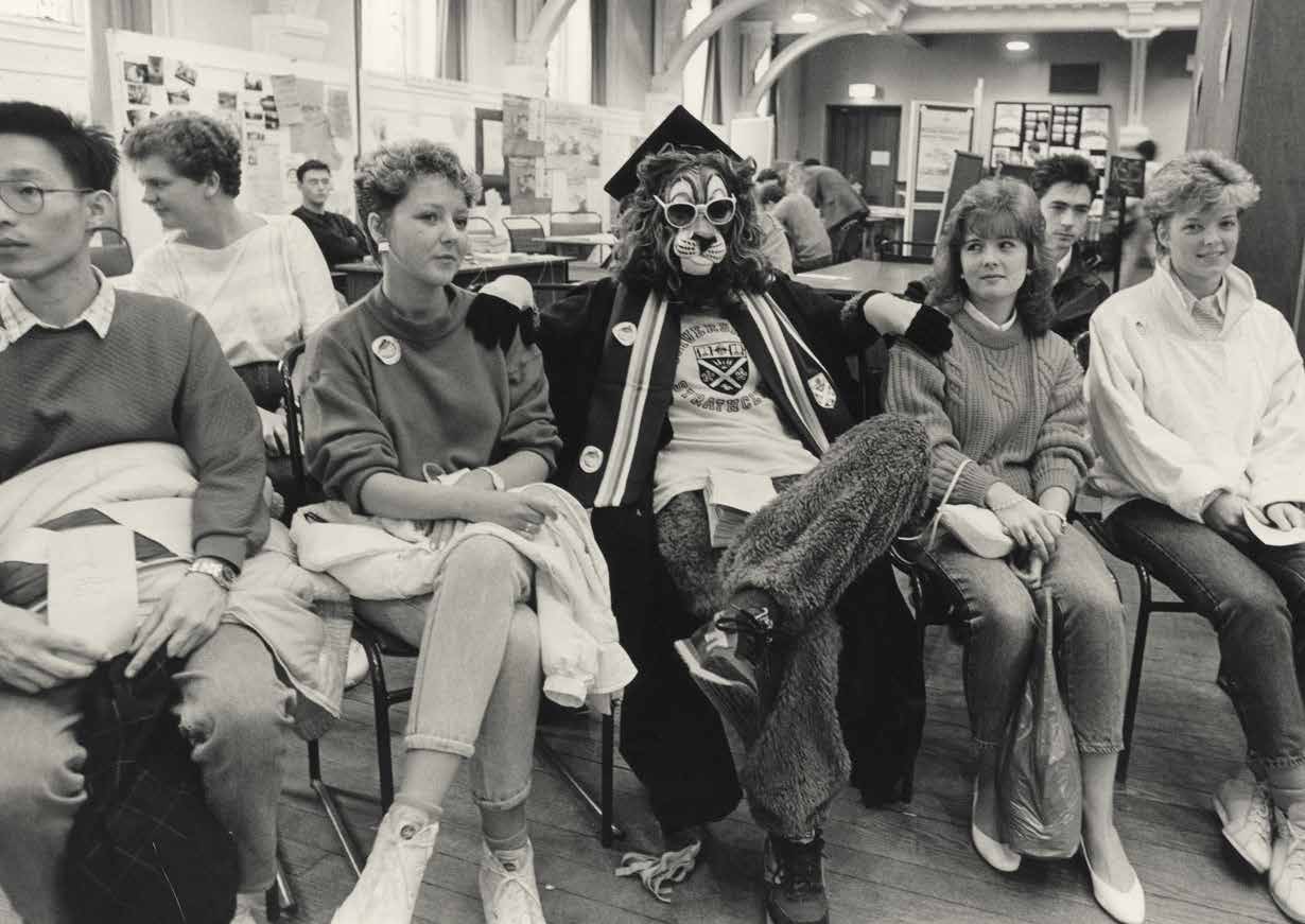 A black and white photograph of the Strathclyde Sports Union mascot sat with four other students