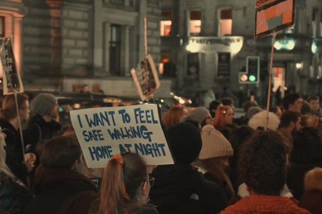 Students walking in the street in the dark holding a sign that says 'I want to feel safe walking home at night'