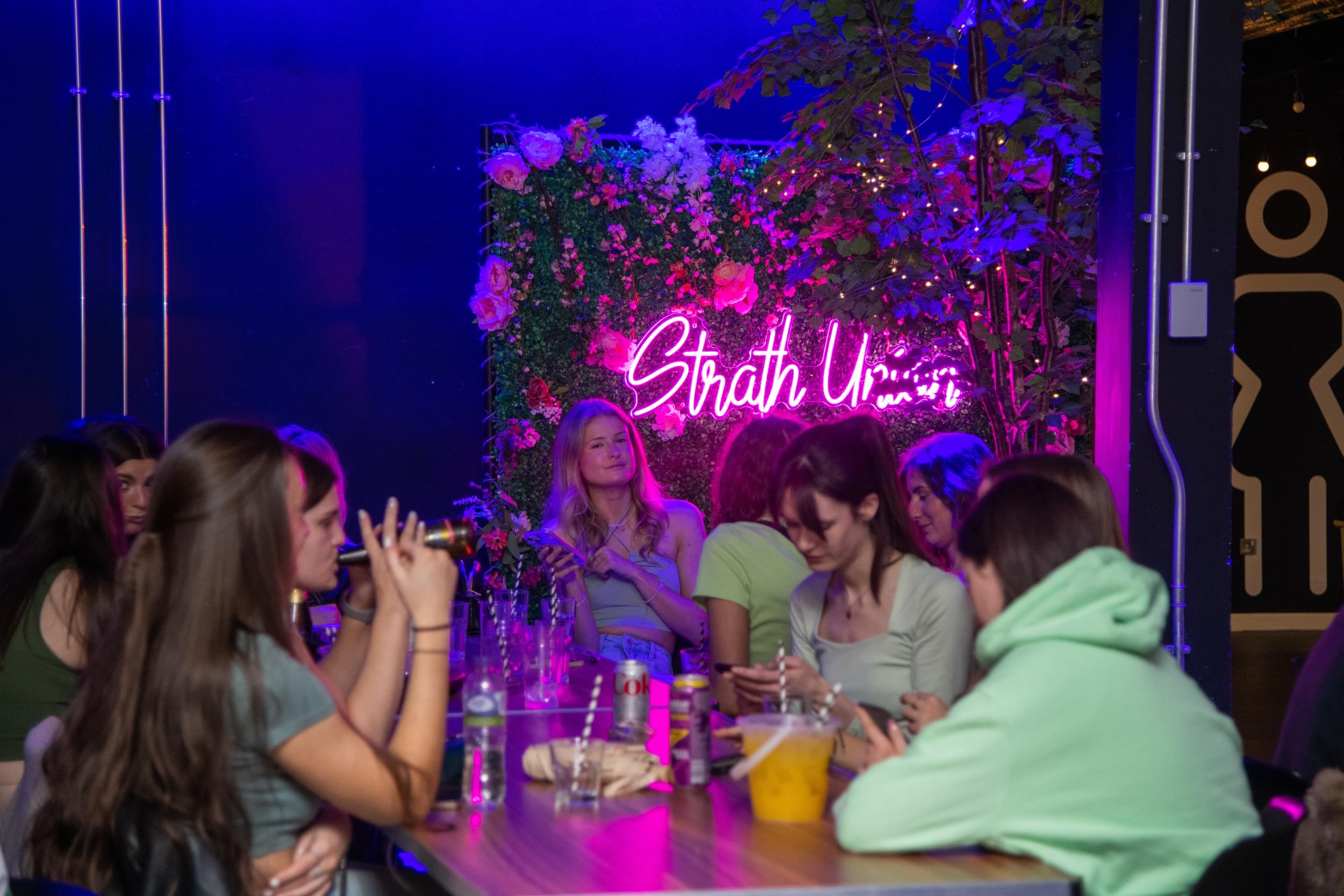 Students sitting at The Terrace in front of the neon Strath Union sign