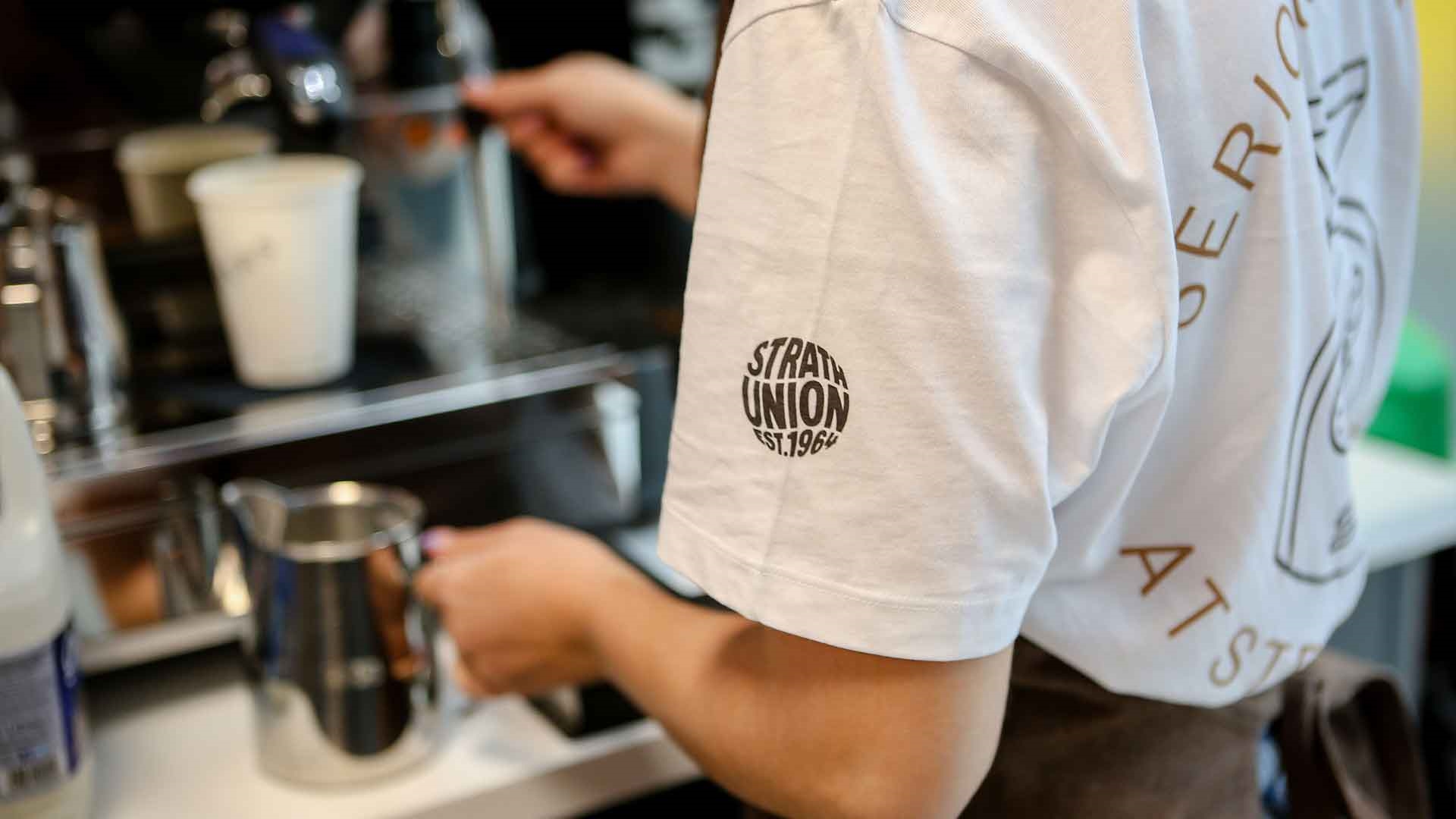 A staff member wearing a white t-shirt with a black Strath Union logo printed on the sleeve