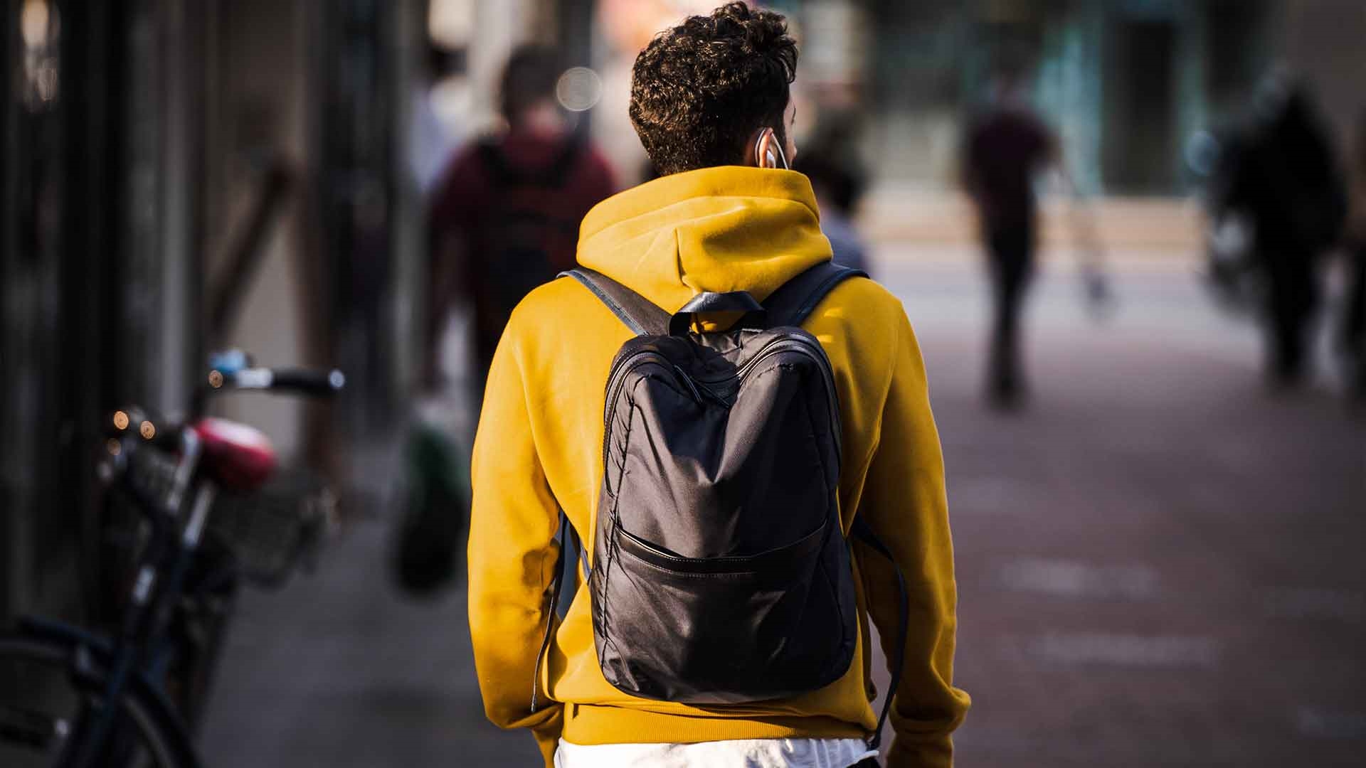 A person walking in the street wearing a yellow sweater and a black backpack