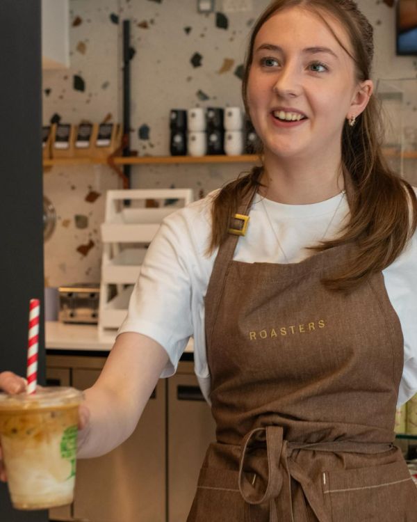 A smiling barista serving iced coffee to customer.