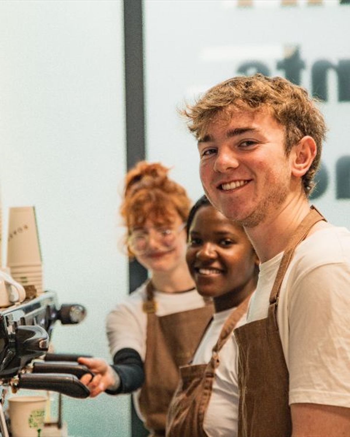 Three Roasters staff members beside coffee machine smiling at camera