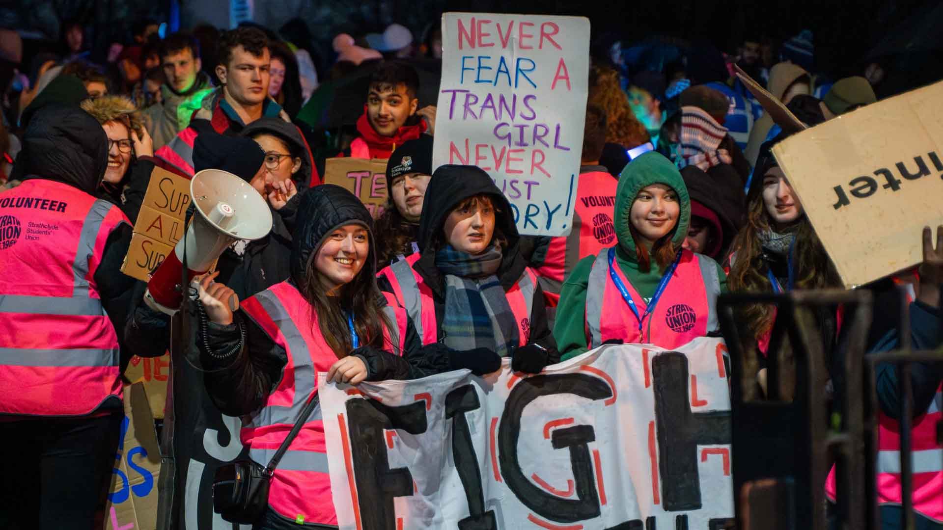 Students, some wearing "Strathclyde Volunteer" vests, holding banners and preparing to march.