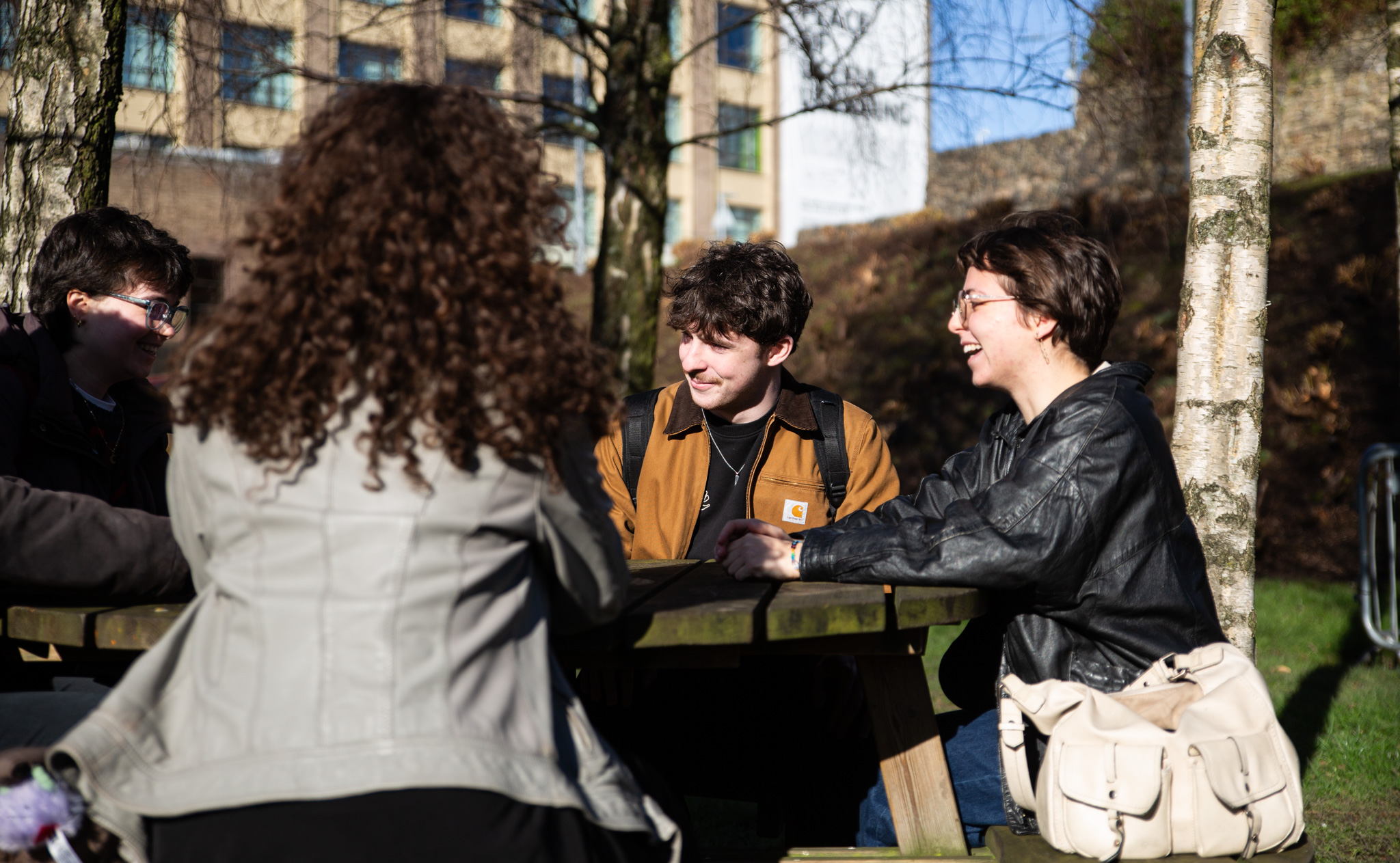 Four students sitting on picnic bench chatting.