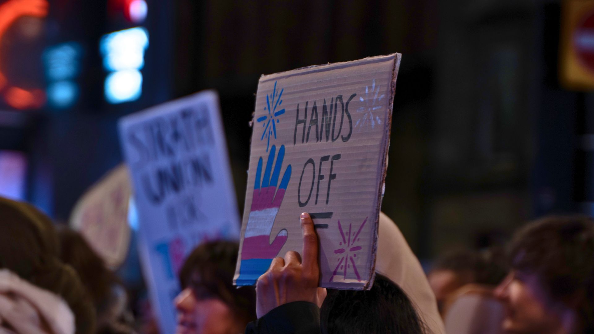 Placard that reads Hands Off using the Trans flag colours.