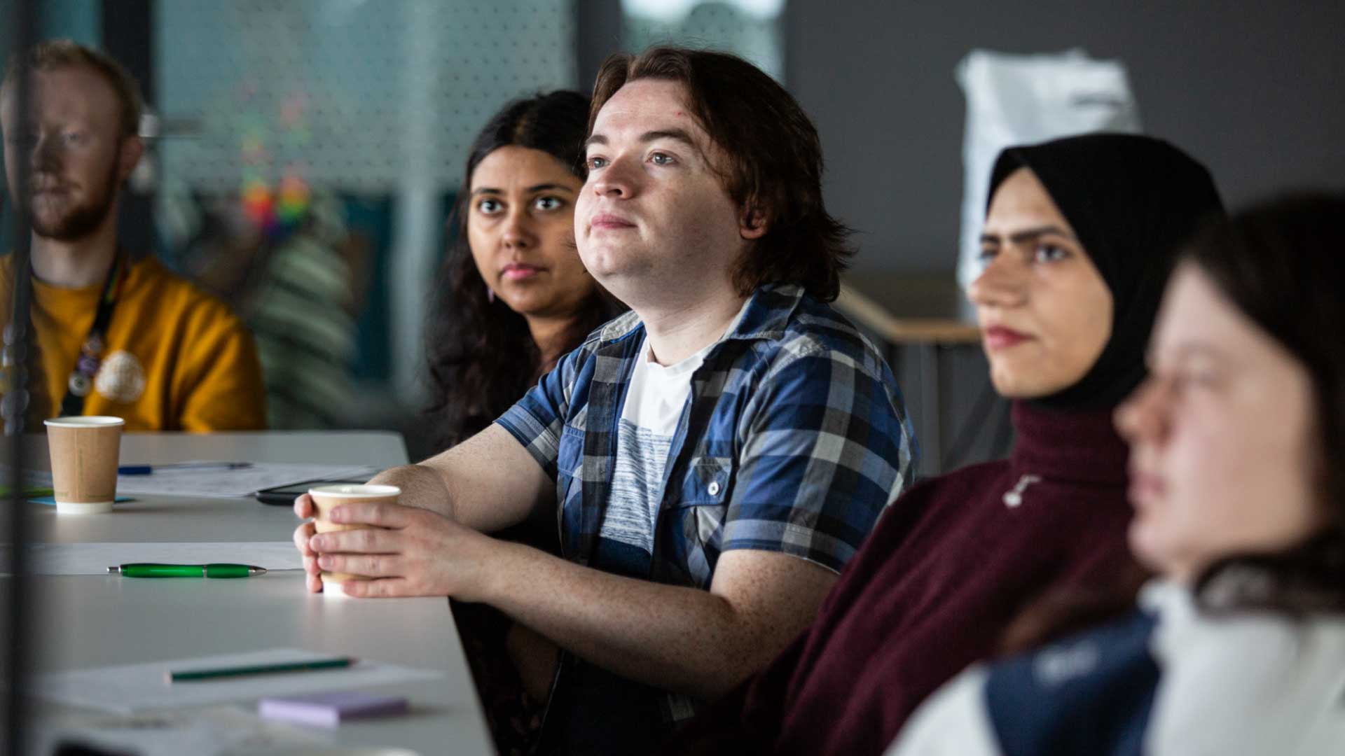 Strathclyde students sitting around a table, listening and looking at someone out of shot.