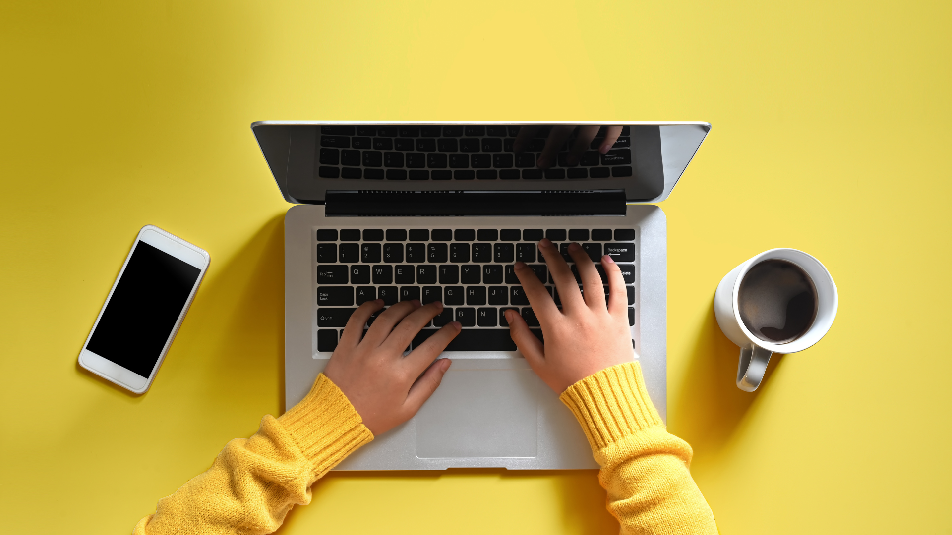 Hands typing on a laptop on yellow background.